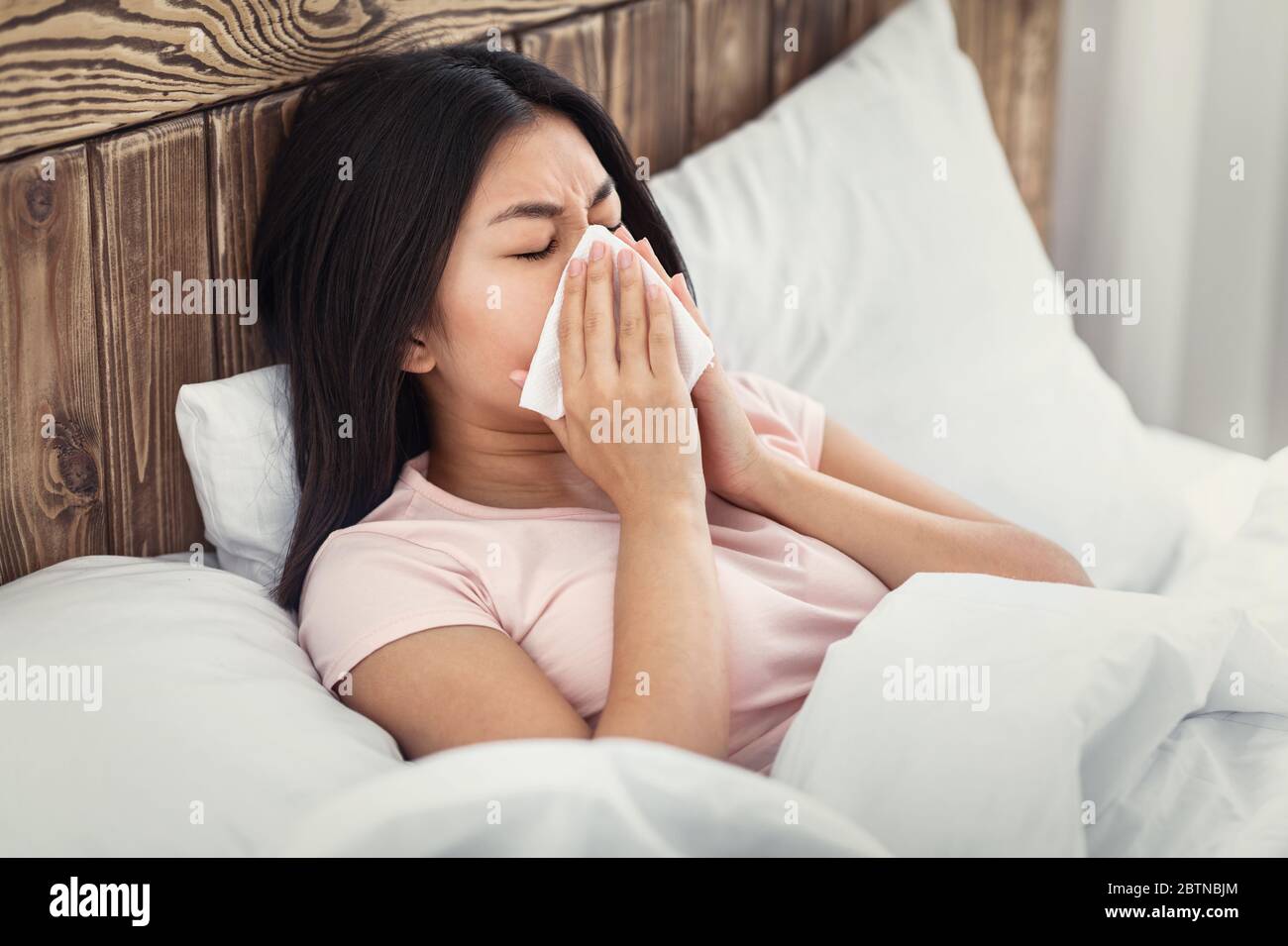 Malade chinoise soufflant nez dans le tissu couché dans le lit Banque D'Images