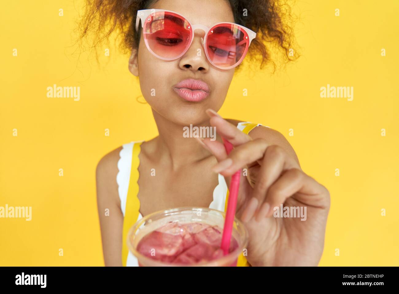 Hipster africain adolescent fille tenant glace boisson porter lunettes de soleil isolé sur jaune. Banque D'Images