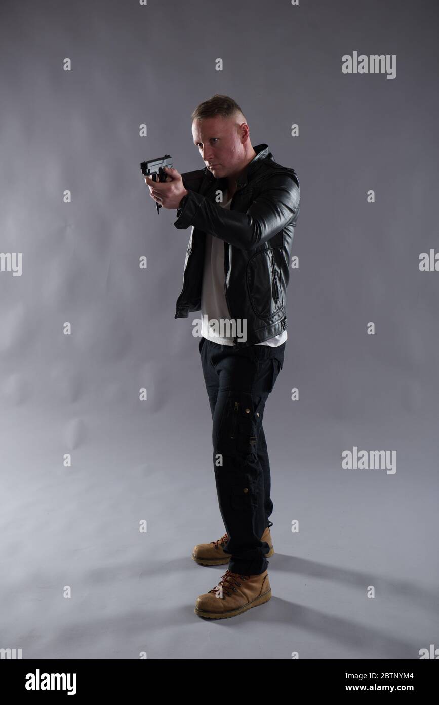 Image isolée d'un homme avec un pistolet portant une veste en cuir noir. Idéal pour les applications de couverture ou de détection telles que la conception de couverture de livre et d'ebook. Banque D'Images