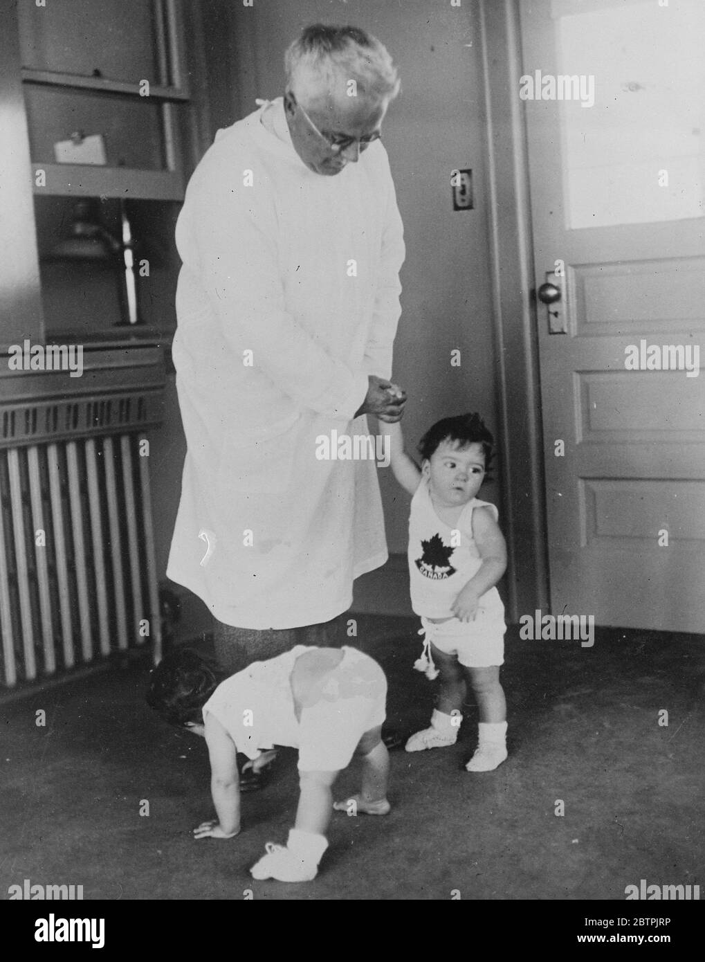 Yvonne vagues triomphalement . Les Quins prennent leurs premiers pas sans aide . Yvonne , avant tout les célèbres quintuplés de Dionne , est le premier à marcher sans aide . Dans un hush à couper le souffle , regardée par le Dr Dafoe et ses infirmières admiratifs , elle a fait ses quelques pas de bébé à travers le plancher de la pépinière , incertaine au début, mais en gagnant la confiance avec chaque foulée . Encouragé par l' exemple de sa sœur , Emelie a suivi , négociant avec succès le parcours difficile à travers la salle de jeux spacieuse de Quins . Photos , Yvonne , Emelie , le second des Quins à marcher sans aide , attend avec impatience de la démarrer Banque D'Images