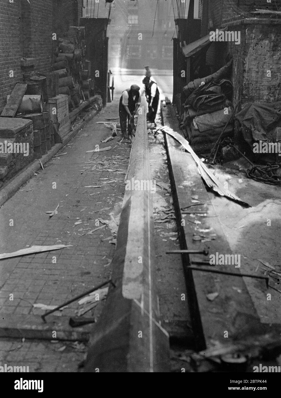 Maître de mât ! . Hache des mâts en bois de 65 pieds de bois brut à London yards . M. Alf Webb , qui a été à l'œuvre pratiquement toute sa vie , hacking deux mâts de 60 pieds en bois d'énormes blocs de bois rugueux s'étendant sur toute la longueur d'une grande cour dans la route du quai ouest indien . Son seul outil est une hache avec laquelle il raque le bois carré de 14 pouces en forme . Une fois terminé, les mâts seront érigés devant les bureaux de l'immeuble de l'Imperial Chemical Industries à Billingham Industries, immense bâtiment de Billingham , Stockton , et chacun portera un drapeau de 16 pieds . Bien que le maki Banque D'Images