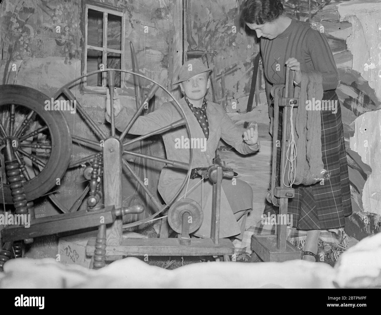 Ann Harding essaie de tourner la roue au salon écossais du textile à Londres . Mlle Ann Harding , l'actrice du film , a ouvert le spectacle écossais textil à la British Industries House , Oxford Street . Une des caractéristiques de l'affichage est le tissage de tartan par M. William Meikle pour répondre à la demande de Coronation . On estime qu'au moins 2 £ , 000 kilts seront portés à la cérémonie de l'abbaye de Westminster . Photos montre , Mlle Ann Harding essaie sa main à la roue qui tourne assistée par Mme William Meikle . 12 mars 1937 Banque D'Images