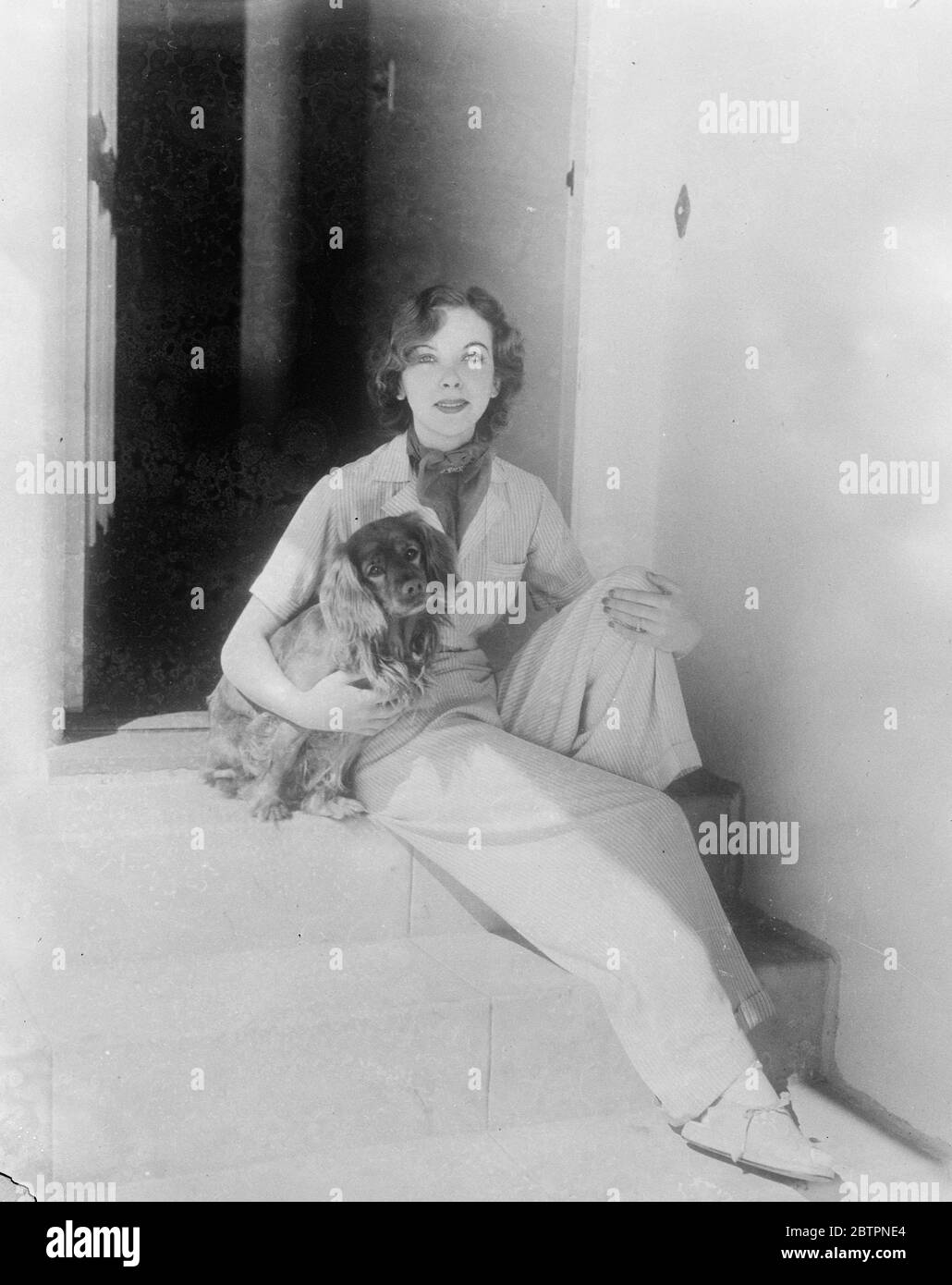 Liberté de mode. Spectacles photo: Portant son nouveau pyjama de plage de mode de matériel rayé, Ida Lupino, l'actrice fille de l'humoriste britannique Stanley Lupino, repose dans le soleil de Californie avec son chien préféré sur les marches de la maison d'Hollywood. 5 juin 1937 Banque D'Images