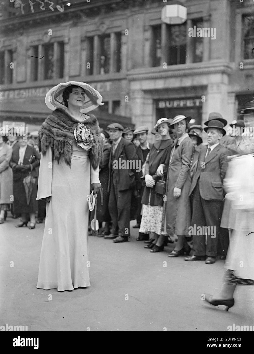 Défilé de mode Ascot à Waterloo. Photos : une femme de course haute dans un grand chapeau et un four cape excite l'admiration d'une galerie alors qu'elle quitte la gare de Waterloo pour le deuxième jour de la réunion d'Ascot. 16 juin 1937 Banque D'Images
