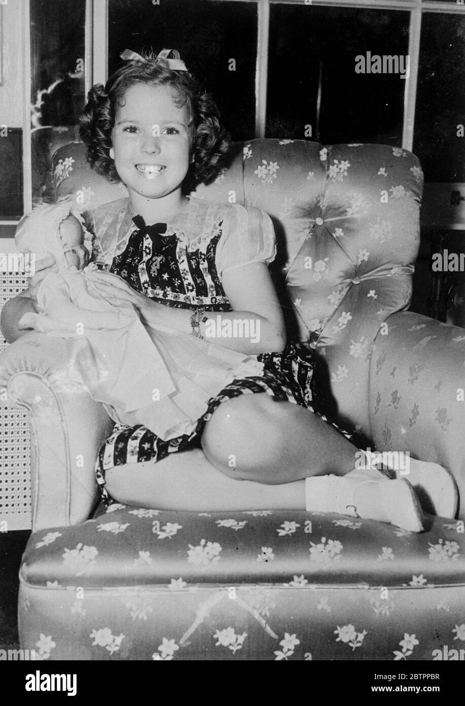 Shirley Temple visite Chicago. Shirley Temple, l'actrice du film pour enfants passe une soirée tranquille avec une poupée dans un fauteuil confortable, à son hôtel lors d'une visite à Chicago. Des arrangements provisoires auraient été faits pour que Shirley visite l'Angleterre dans un avenir proche. Banque D'Images