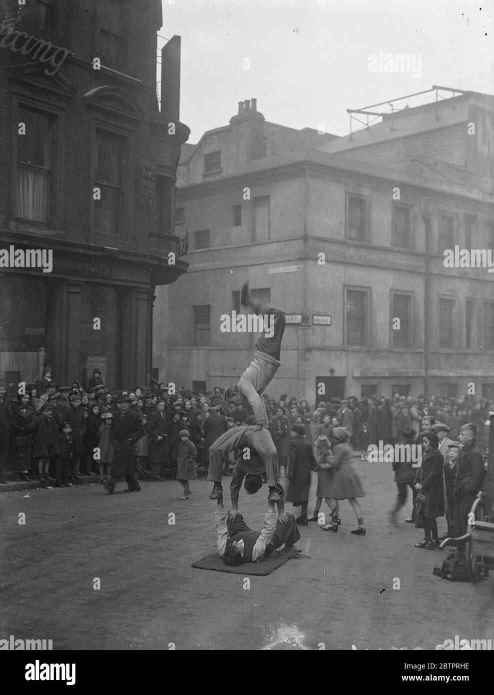 Le théâtre est le pavé. Des acrobates au bord du trottoir, offrant un divertissement supplémentaire pour la foule de personnes qui attendent d'entrer dans le Lyceum Theatre, Londres, pour voir le pantomime « Beauté et la Bête » le lendemain de Noël, le jour férié, qui suit le jour de Noël. Les artistes de la rue, notamment les chanteurs, les danseurs et les comédiens, sont un élément bien établi de la vie théâtrale de Londres. Comme les places moins chères dans la fosse et la galerie du théâtre de Londres ne peuvent pas être réservées, de longues files d'attente de personnes attendaient dehors pour s'assurer des meilleures places quand le théâtre ouvre ses portes. Les longues heures d'attente Banque D'Images