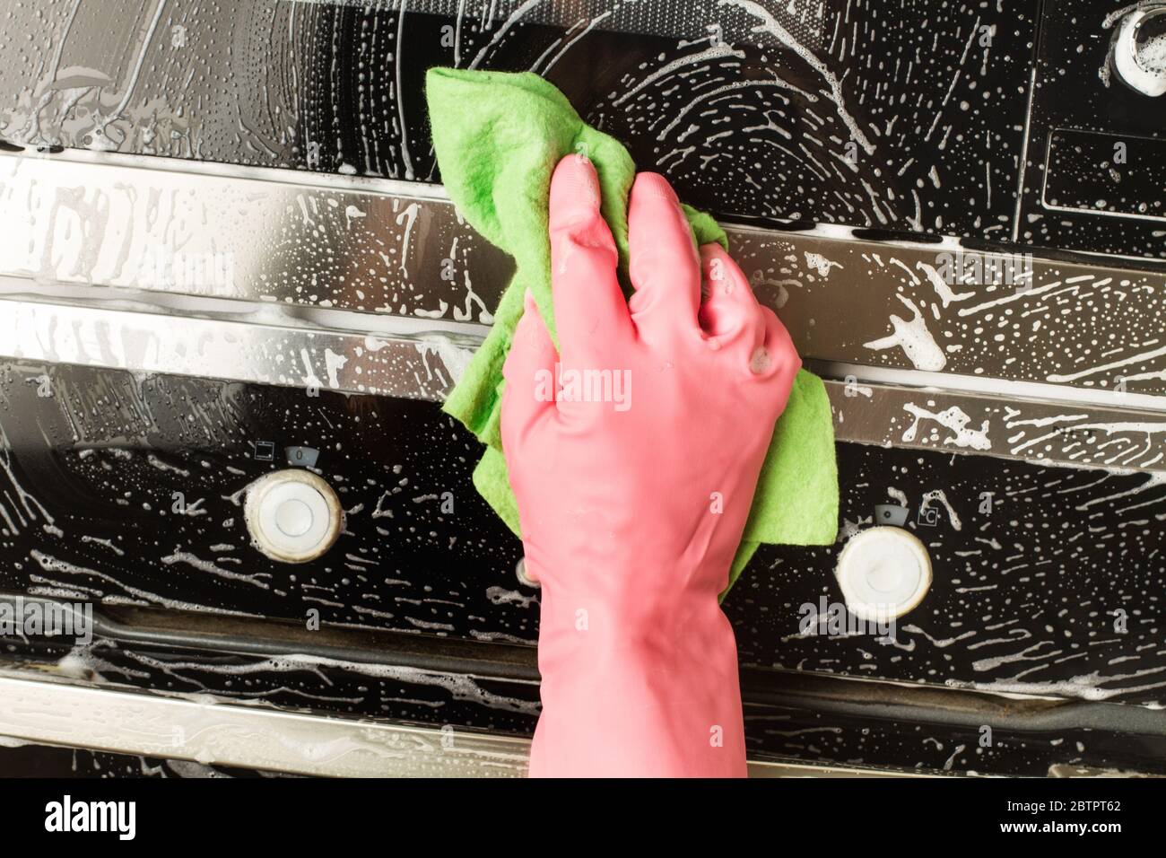 Homme avec des gants en caoutchouc et une éponge de nettoyage four et porte de micro-ondes Banque D'Images