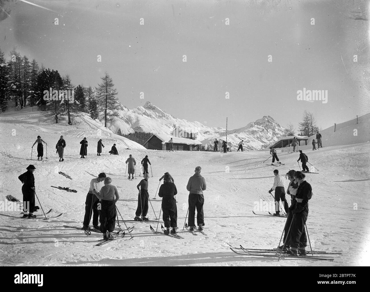 Ski dans les montagnes enneigées. De longues ombres plantées sur la neige, les skieurs se sont mis en route pour le sport de la journée entouré de montagnes aux sommets blancs et d'arbres enneigés à St Moritz, la station suisse météo la saison des sports d'hiver a ouvert. 25 décembre 1937 Banque D'Images