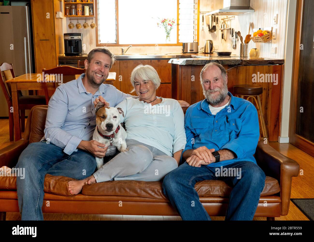 Famille d'un homme adulte et de parents âgés se détendant aimant leur chien mignon en appréciant le temps ensemble de se détendre sur le canapé. Image positive de la vie à la maison Banque D'Images