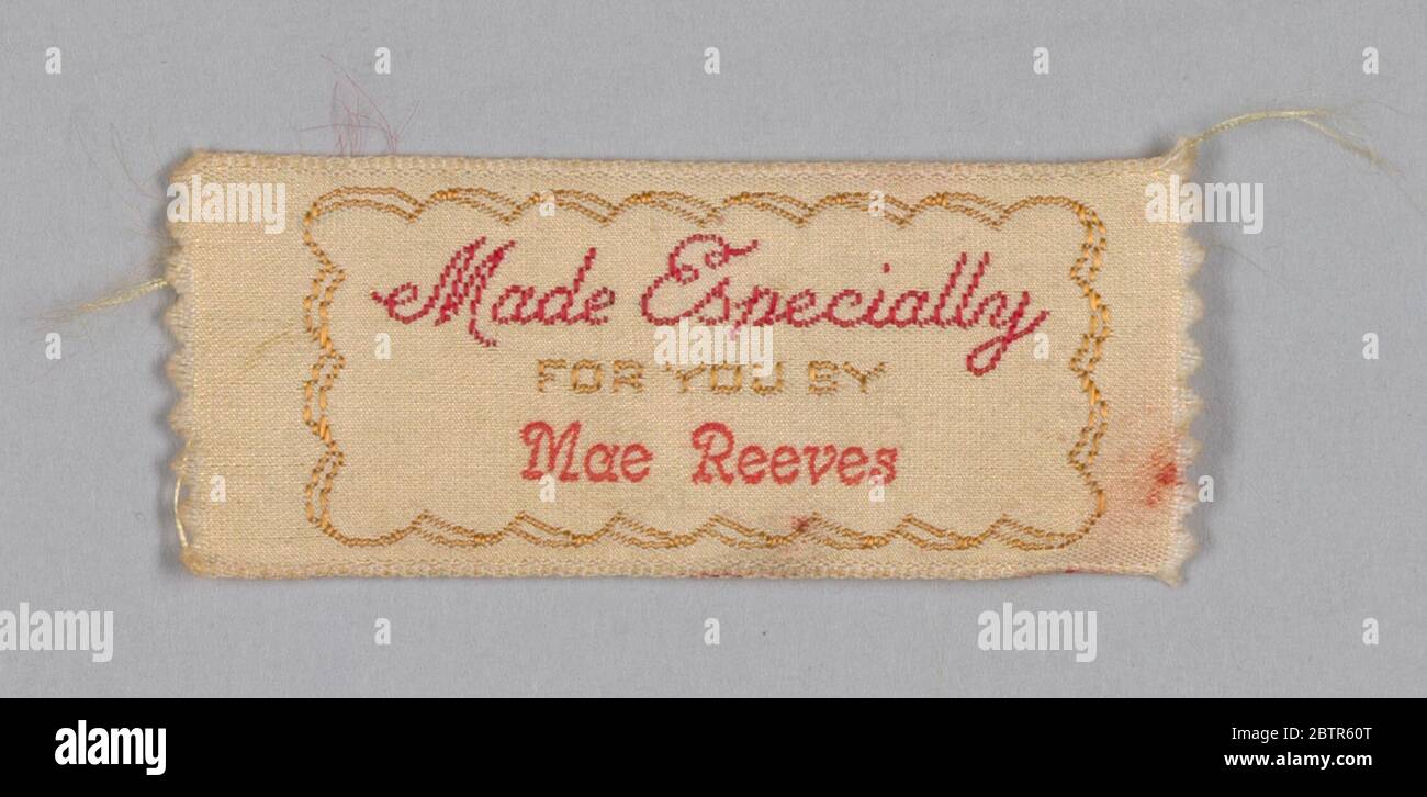 Deux étiquettes de vêtements pour Mae Reeves de la boutique de la Millinery de Maes. Deux étiquettes identiques en soie crème avec broderie machine de fil de soie en bordeaux et or qui se lit 'Made spécialement / FOR YOU BY'. Sous la broderie, le nom « ae Reeves » est estampillé à l'encre rouge. Une bordure en or festonné entoure le texte. Banque D'Images