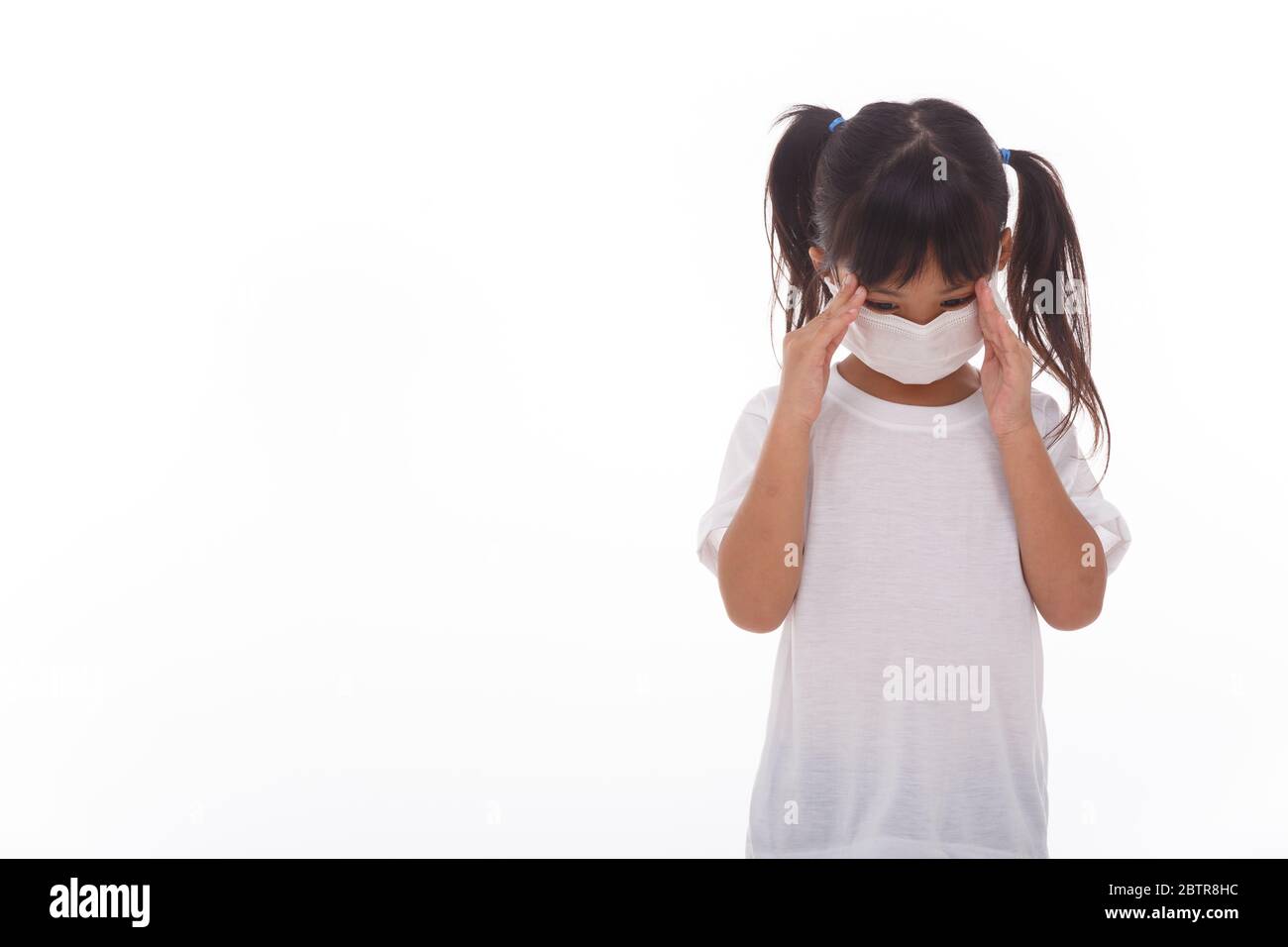 Un enfant asiatique portant un masque médical ressent des maux de tête sur fond blanc. Banque D'Images