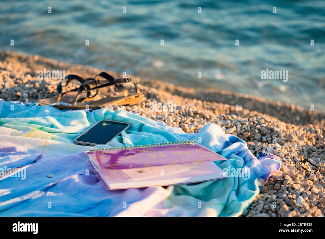 Ordinateur portable, téléphone portable, sandales pour femmes et serviette de plage sur une plage rocheuse Banque D'Images