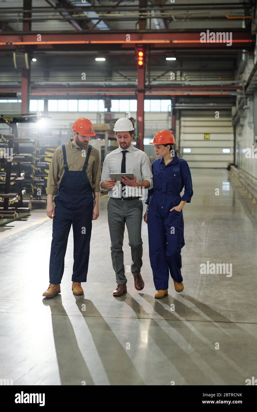 Directeur industriel discutant de la production avec les employés tout en analysant les données sur tablette et en parcourant l'atelier Banque D'Images