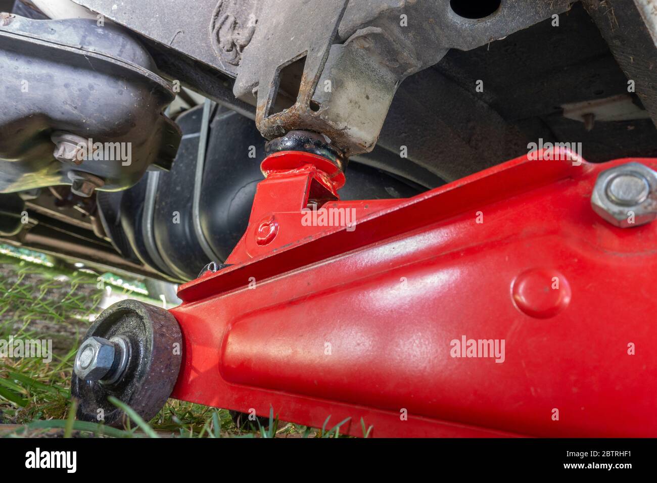 Gros plan d'un cric rouleur hydraulique à usage intensif au sol sous une fourgonnette, relié à un point de levage, avec le véhicule soulevé. Banque D'Images