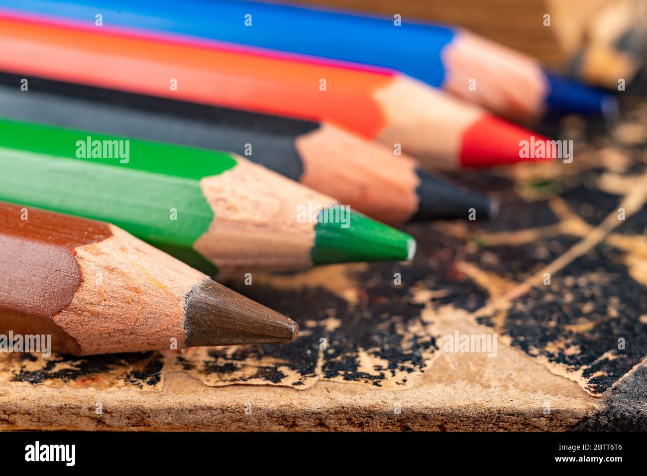 Crayons de couleur sur un vieux livre. Anciens accessoires pour colorier et dessiner dans la bibliothèque. Arrière-plan sombre. Banque D'Images