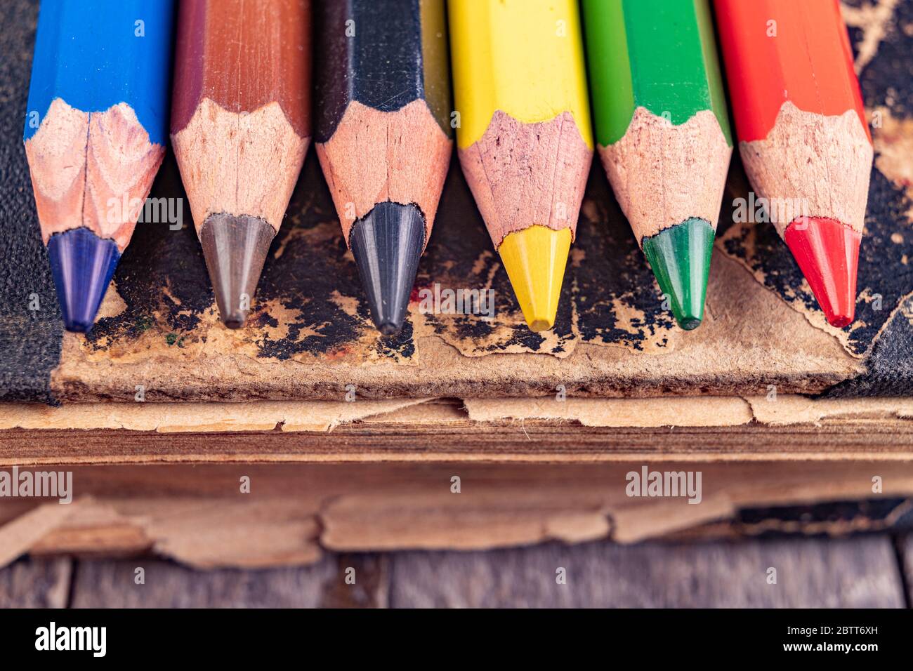 Crayons de couleur sur un vieux livre. Anciens accessoires pour colorier et dessiner dans la bibliothèque. Arrière-plan sombre. Banque D'Images