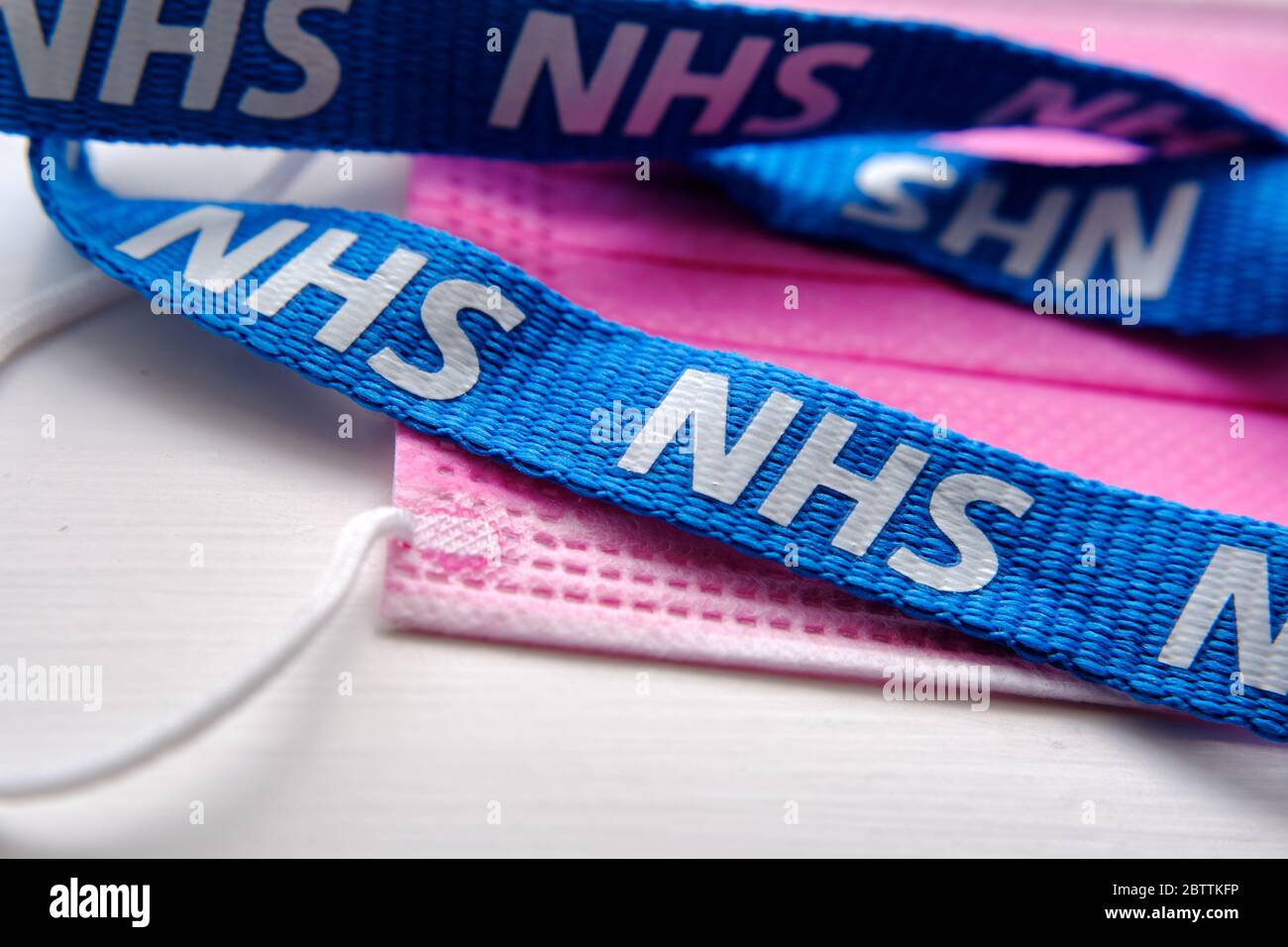 De grandes lettres NHS sont visibles sur le cordon bleu qui est placé sur un masque antiviral rose. Concept de lutte contre la pandémie COVID-19. Banque D'Images