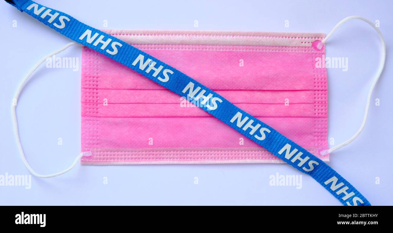 De grandes lettres NHS sont visibles sur le cordon bleu qui est placé sur un masque antiviral rose. Concept de lutte contre la pandémie COVID-19. Banque D'Images