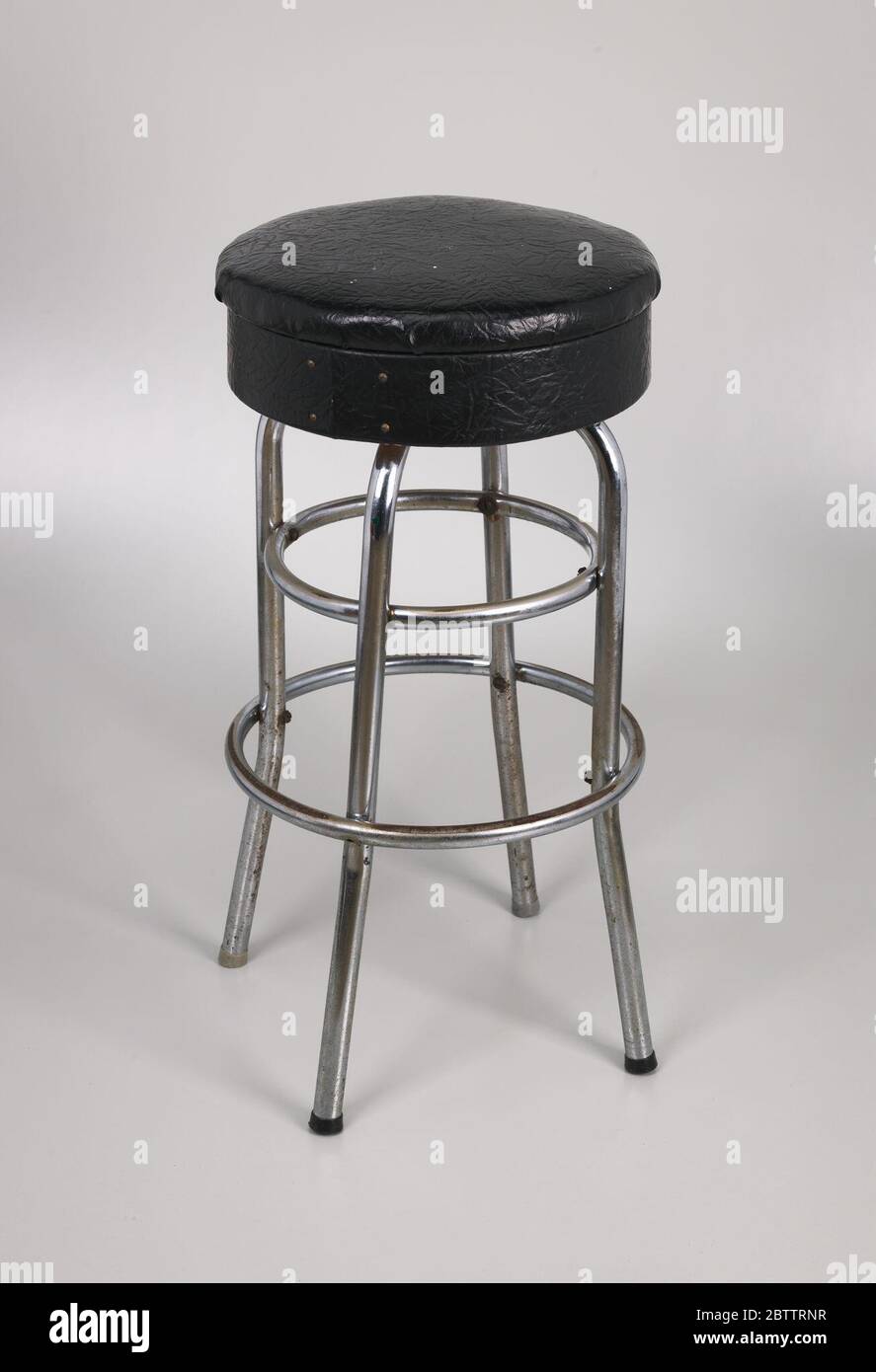 Tabouret avec une couverture en vinyle noir de Muse Bar le bar d'Isaïe Muse. Un tabouret de bar en métal avec un siège en vinyle noir. Le siège du tabouret est constitué de deux (2) sections de siège qui se fixent ensemble. La partie supérieure du siège est un morceau de mousse d'environ 1-1/2 po d'épaisseur recouvert de vinyle noir. Banque D'Images