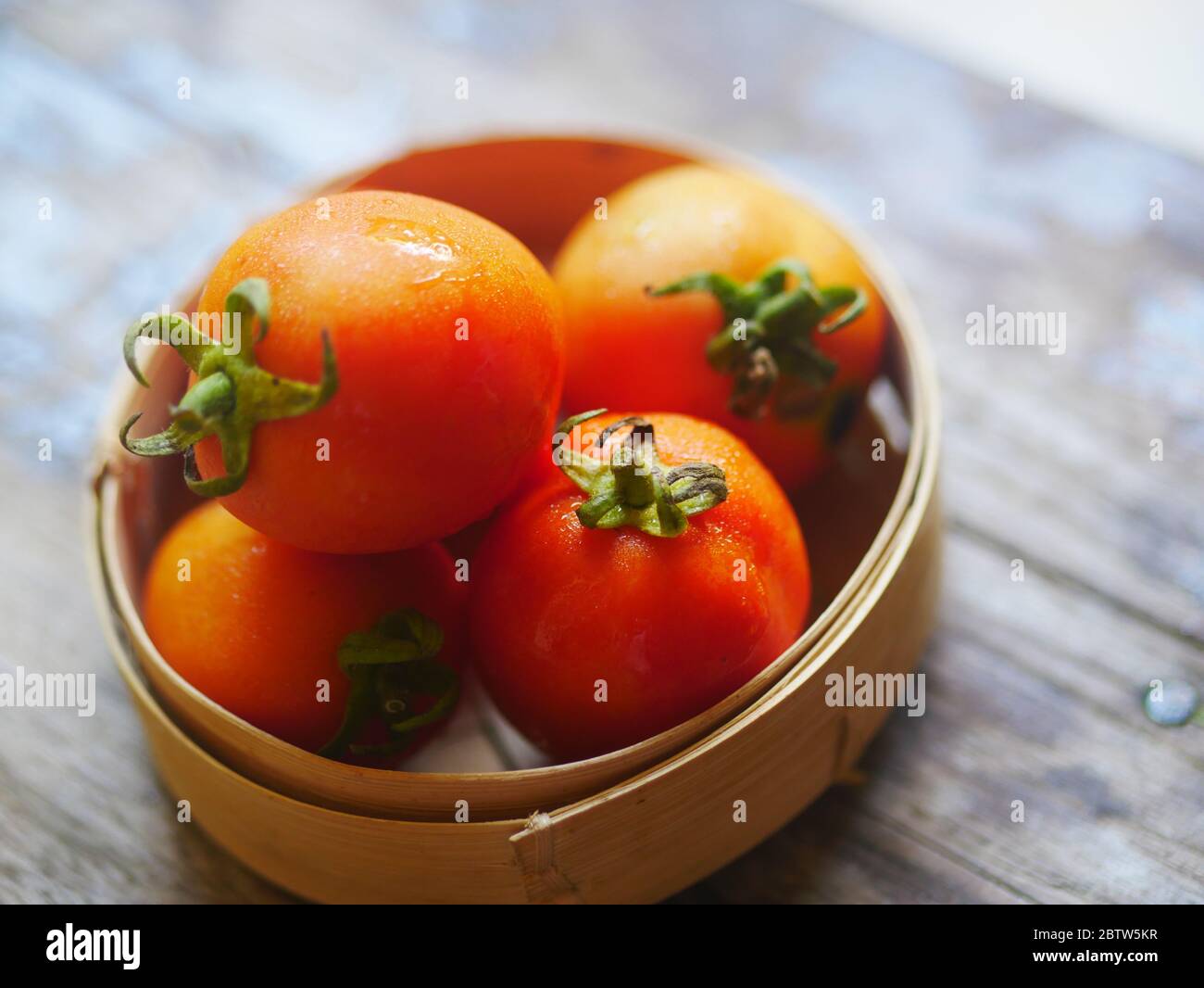 Tomates dans un panier en bambou sur une table en bois. Banque D'Images