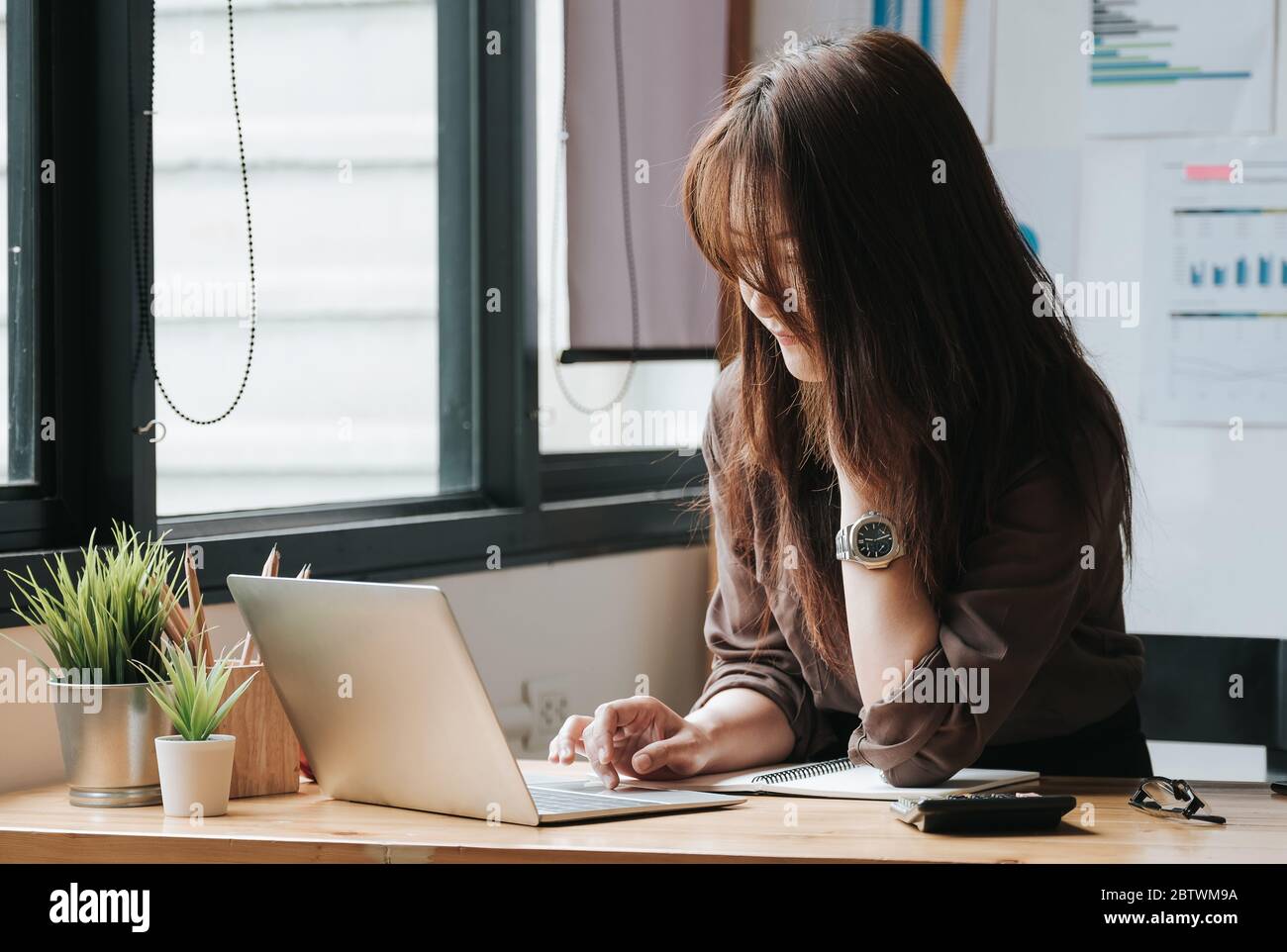 Femme d'affaires utilisant un ordinateur portable et une calculatrice pour faire des finances mathématiques sur un bureau en bois dans le bureau Banque D'Images