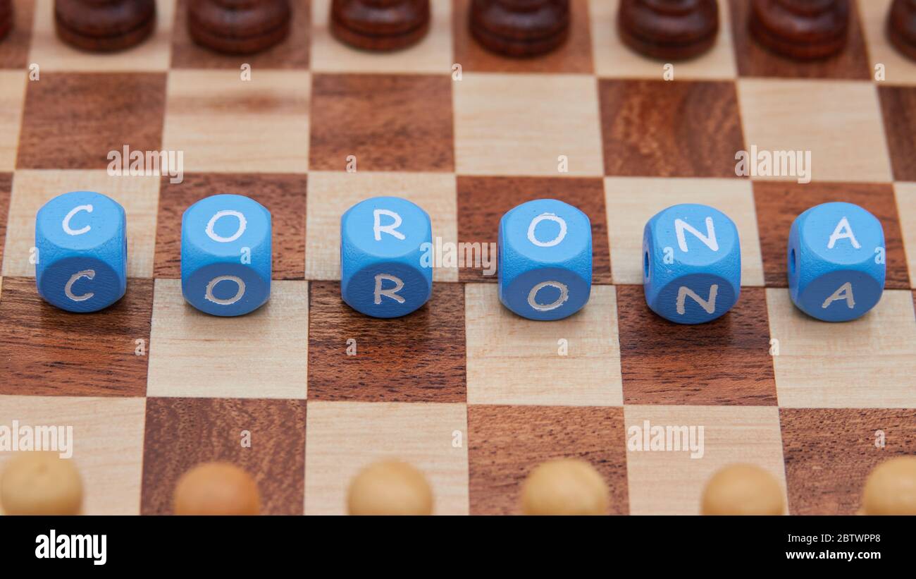 Pièce d'échecs pion noir et blanc, face l'un à l'autre sur un petit plateau d'échecs, au milieu il y a des cubes de lettre, qui forment le mot Corona. Banque D'Images