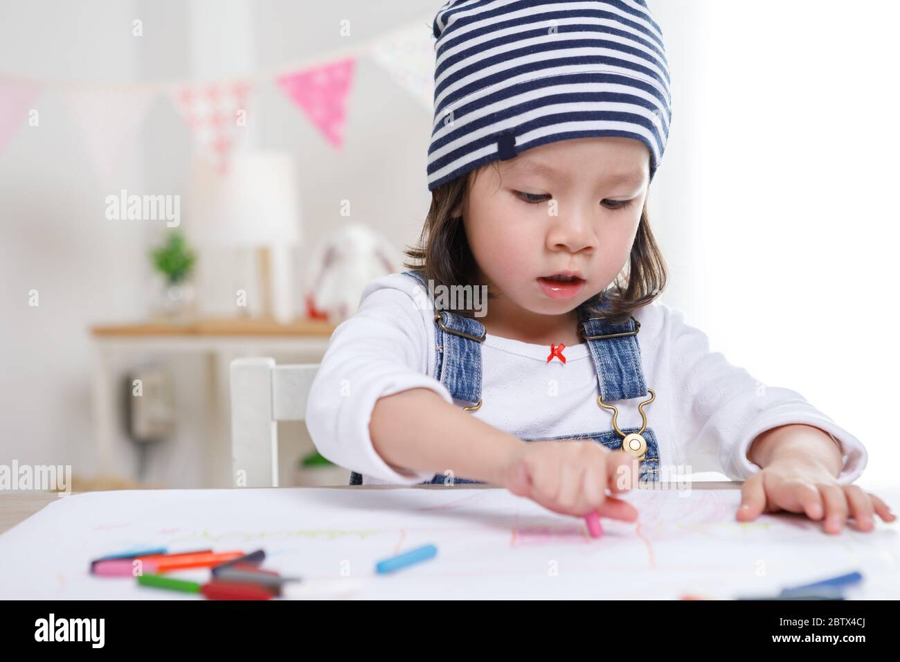 Petite fille asiatique assise à une table dans la chambre, fille Preschooler dessin sur papier avec des stylos colorés sur jour ensoleillé, maternelle ou de garde de jour. Éducation Banque D'Images