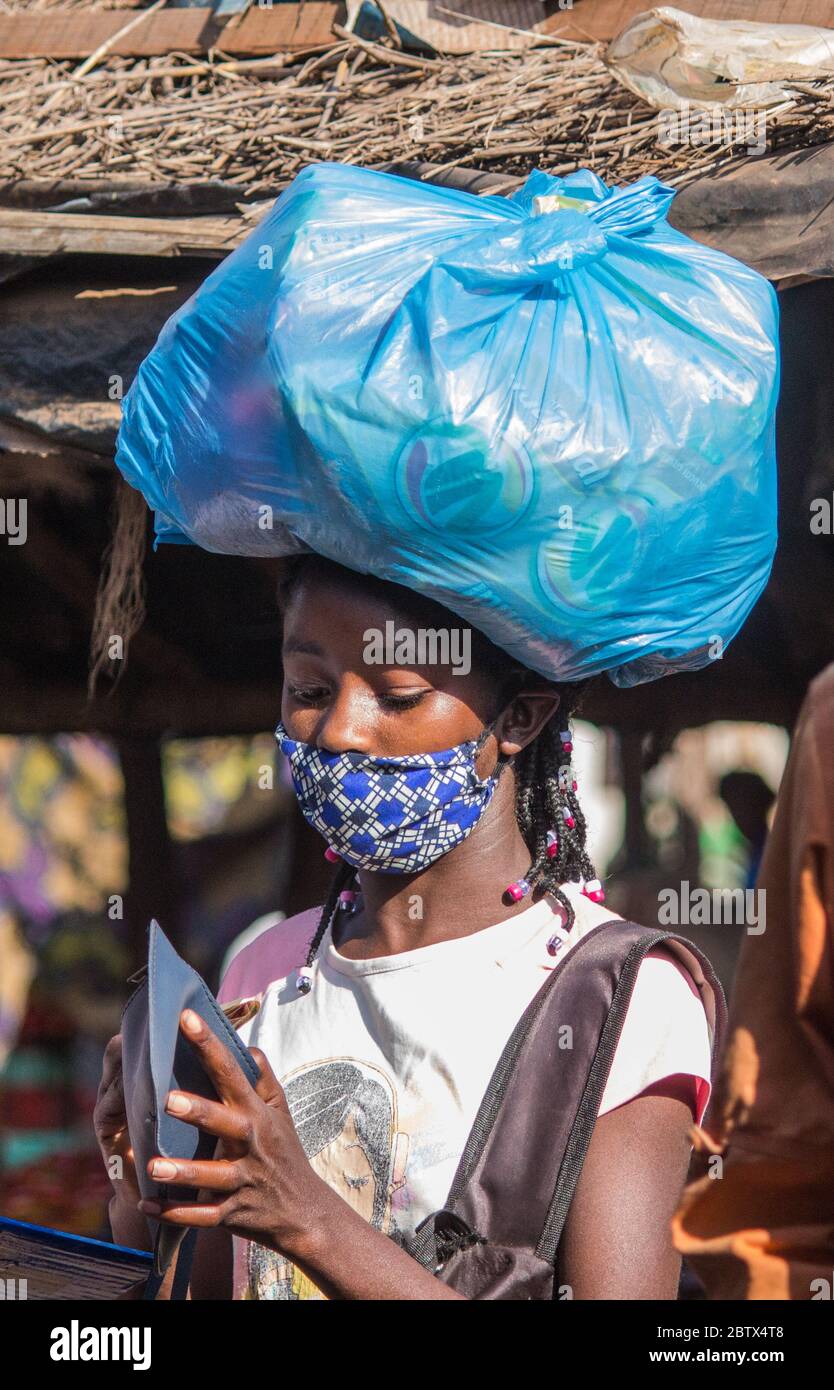 Fille portant un sac en plastique shopping sur sa tête, portant un masque facial en tissu sarong africain pour la protection contre le virus corona Banque D'Images