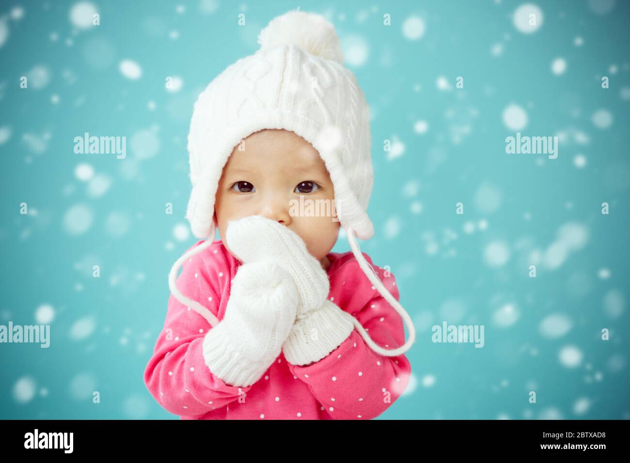 Bébé avec chapeau de coolé blanc et moufles tricotées avec chute de neige Banque D'Images