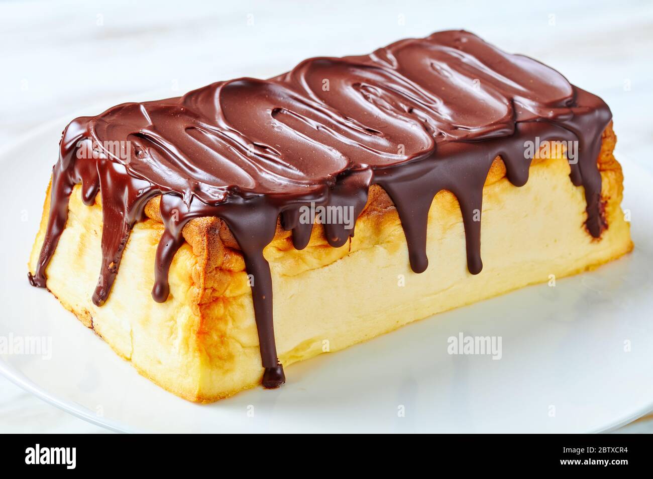 Cheesecake de fromage cottage ukrainien avec raisins secs et glaçage au chocolat noir servi sur une assiette blanche sur fond de bois blanc, gros plan Banque D'Images
