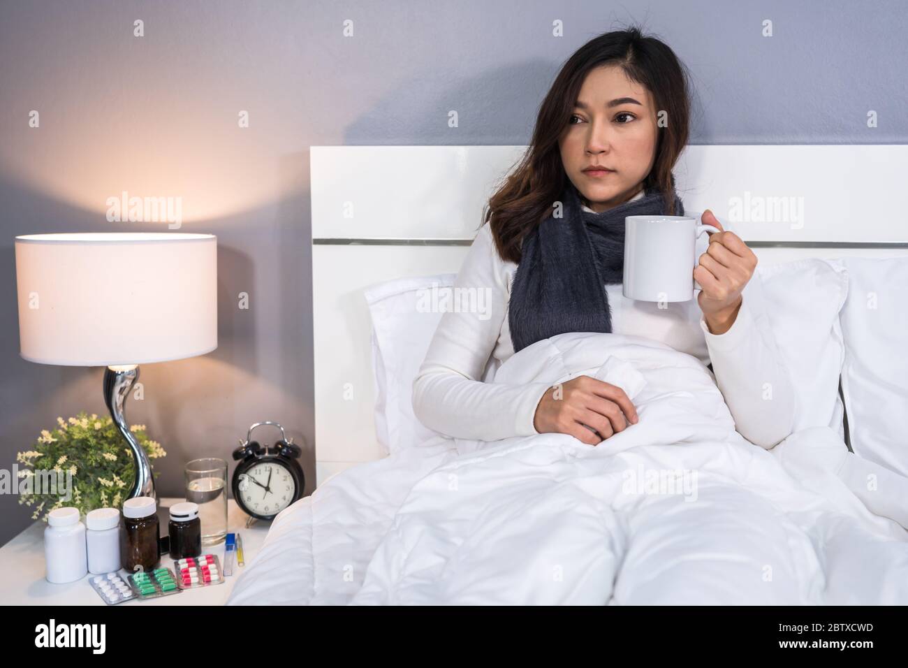 femme malade buvant une tasse d'eau chaude sur un lit Banque D'Images