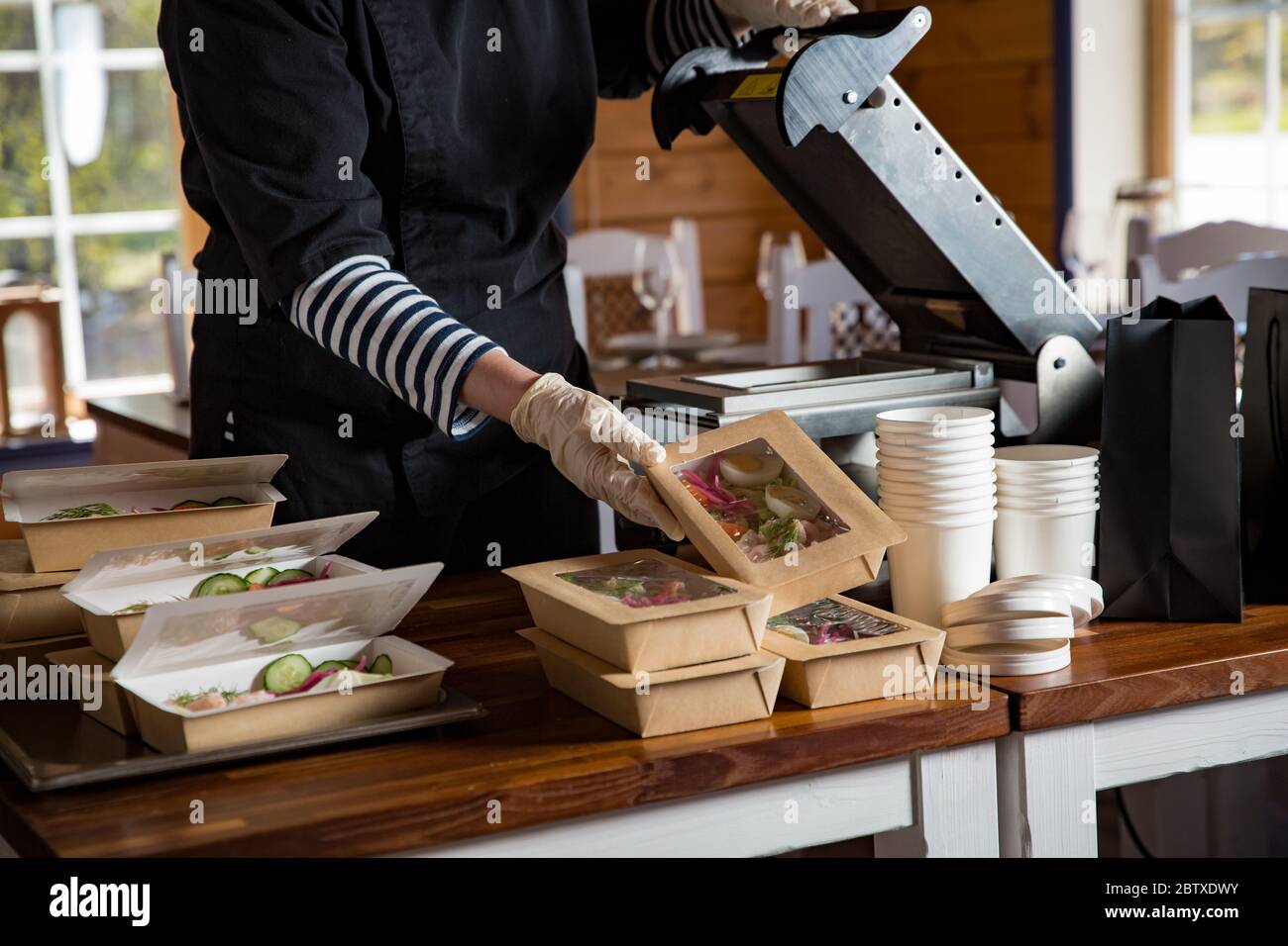 Employé de restaurant portant un masque de protection et des gants emballant les aliments en boîte à emporter. Services de livraison de nourriture et achats alimentaires sans contact en ligne. Banque D'Images