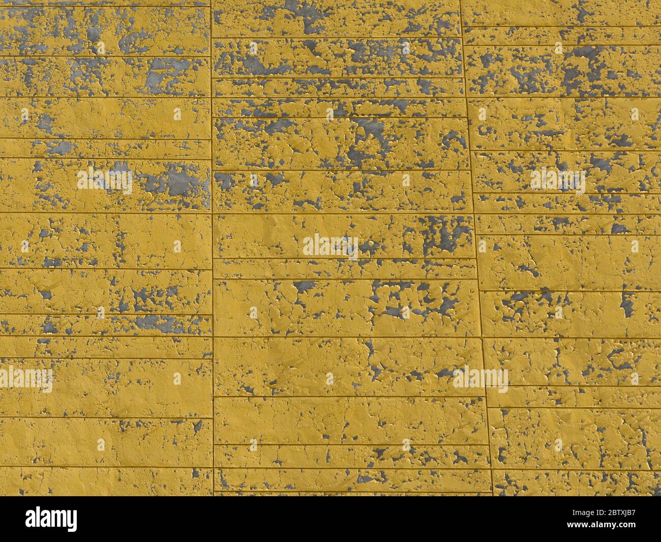 Peinture jaune éraflée et rayée sur un mur en béton. Texture rugueuse. Gros plan d'une façade de bâtiment. Banque D'Images