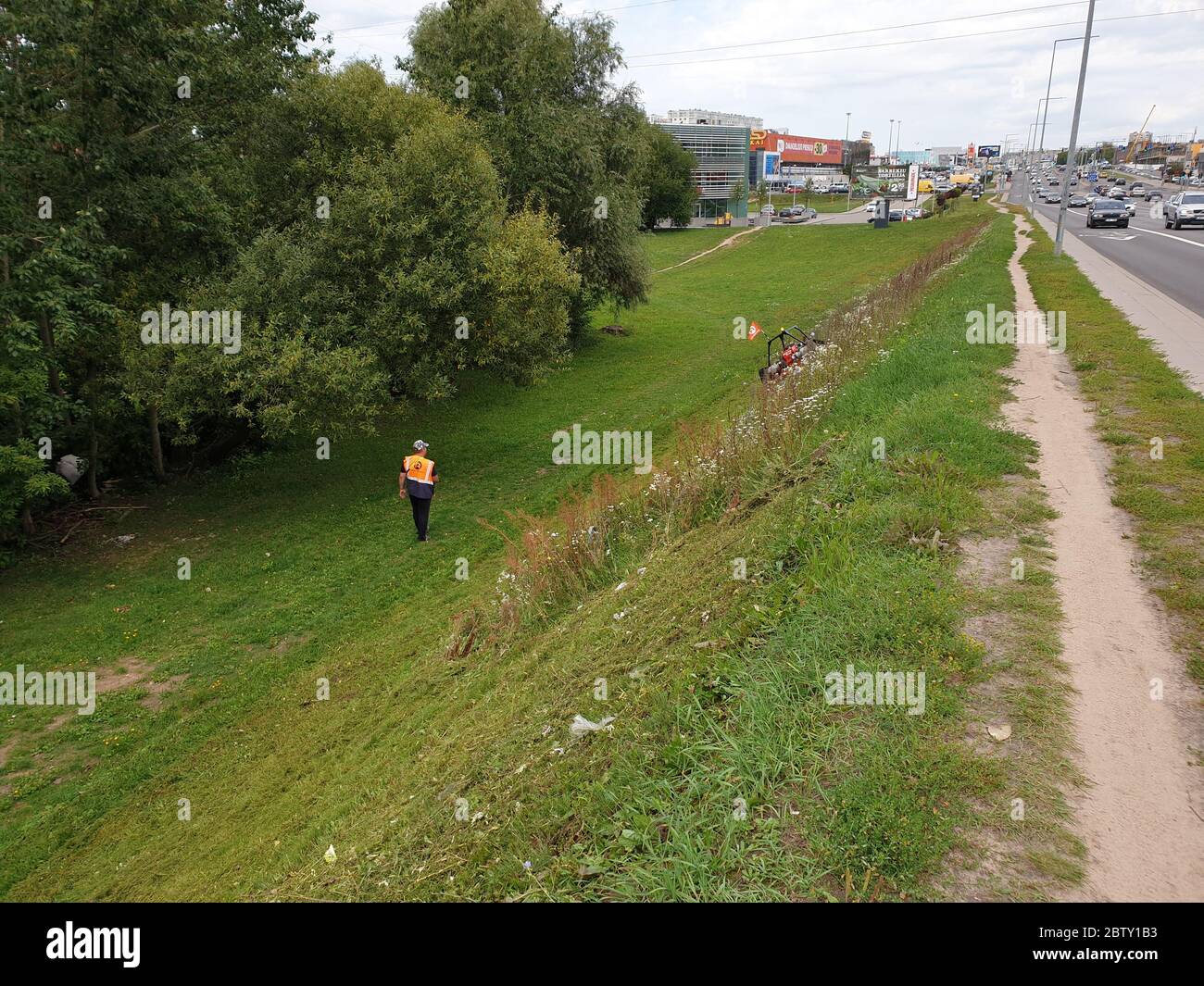 Un travailleur qui coupe de l'herbe sur la falaise avec une tondeuse à distance Banque D'Images