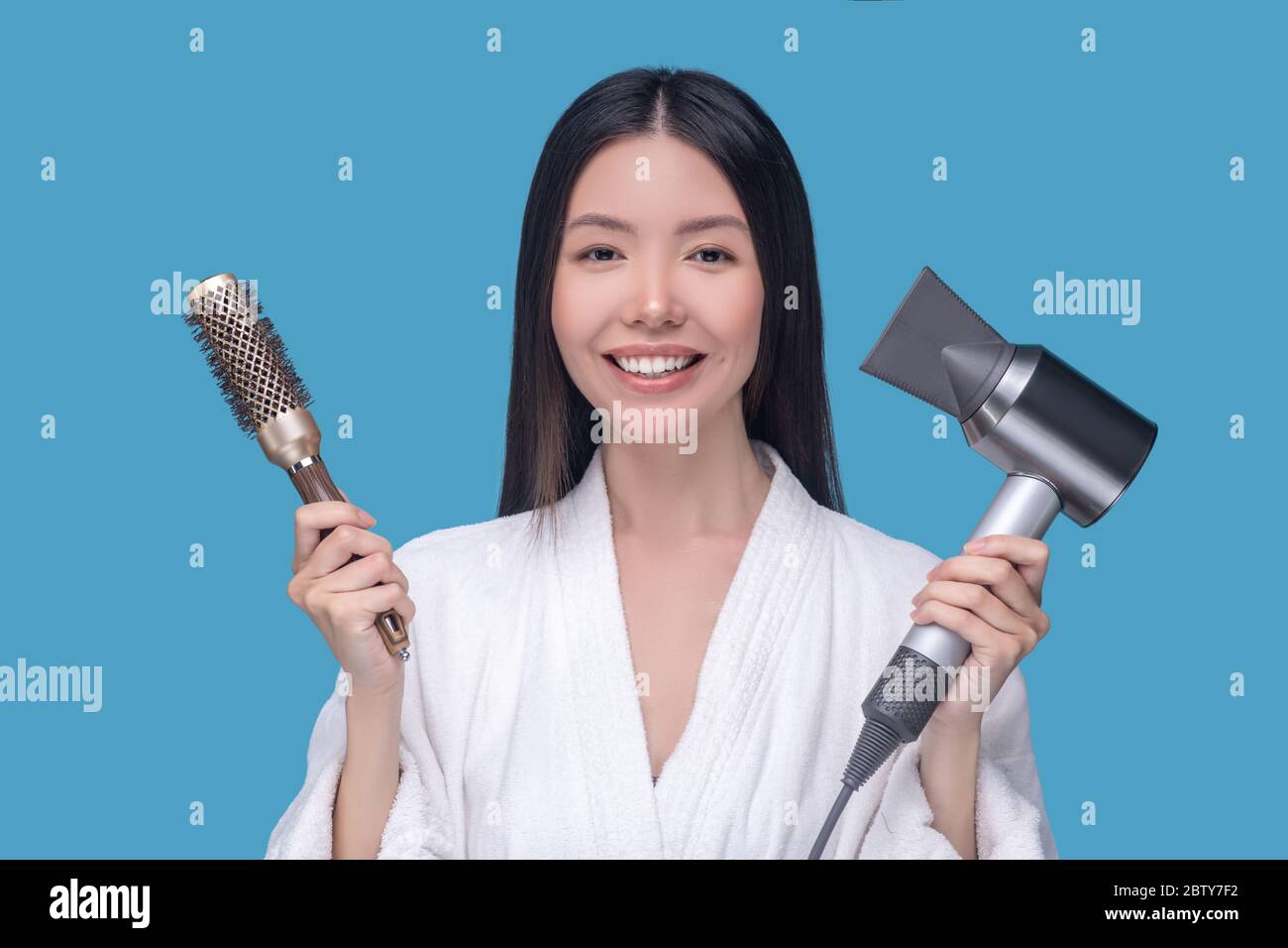 Brunette jeune femme asiatique tenant une brosse et un sèche-cheveux Banque D'Images
