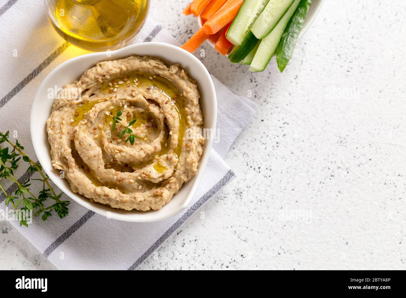 sauce houmous dans un bol, graines de sésame, huile d'olive, concombre et carottes sur fond clair Banque D'Images