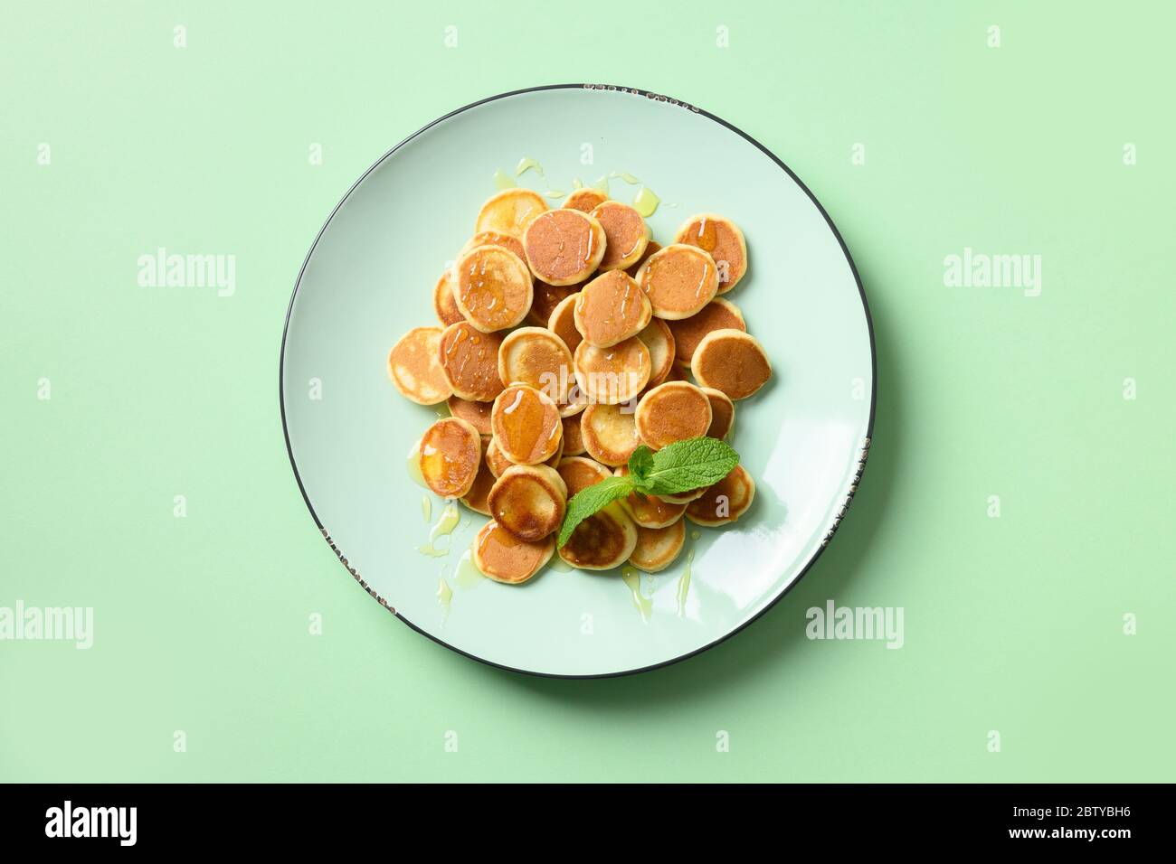 Petites crêpes aux céréales faites maison avec du miel dans une assiette verte sur fond turquoise. Vue de dessus. Petit déjeuner enfant savoureux. Banque D'Images
