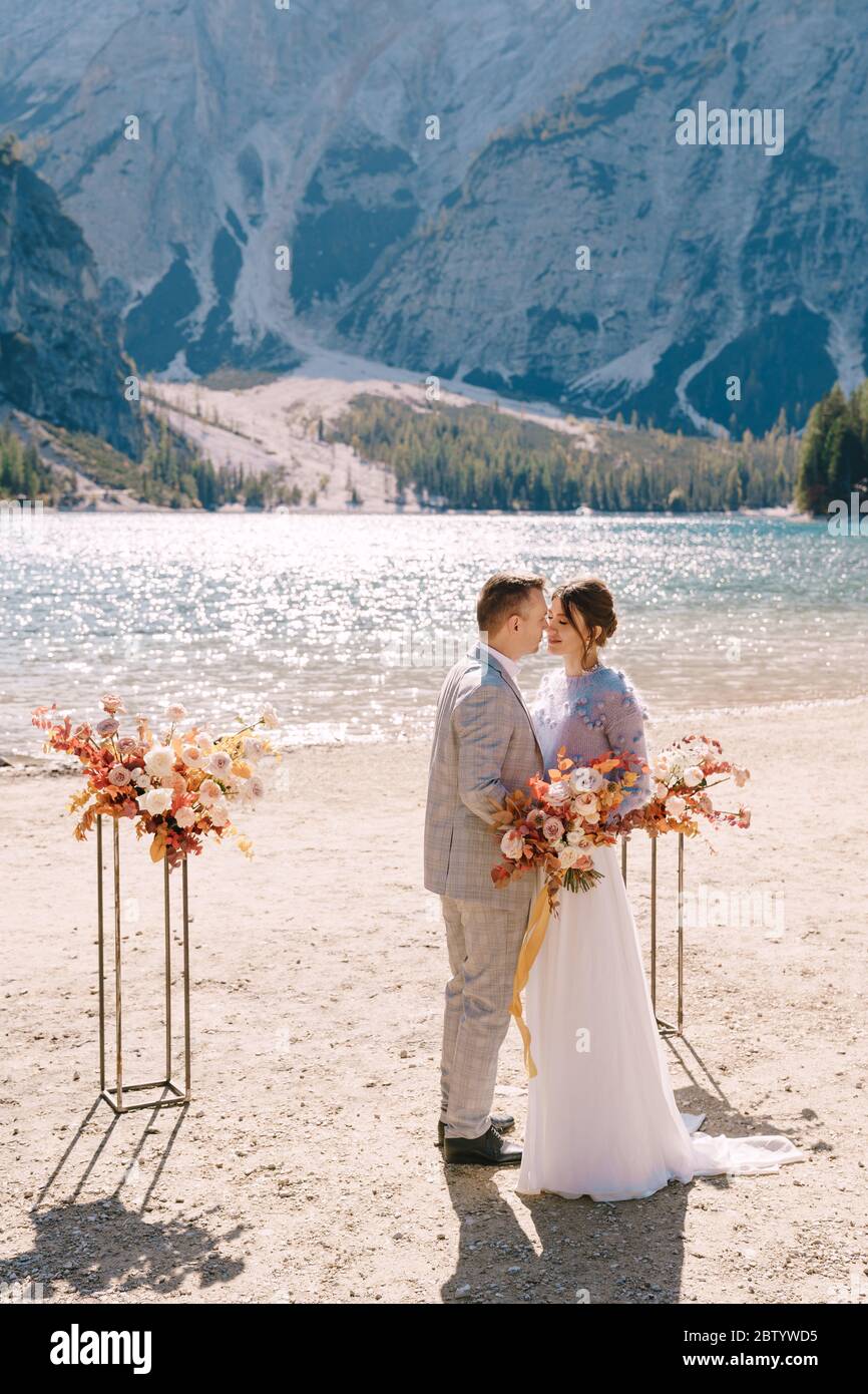 Le marié met un anneau à la mariée, au lieu de la cérémonie, avec une arche de colonnes de fleurs d'automne, sur fond de Lago di Braies dedans Banque D'Images