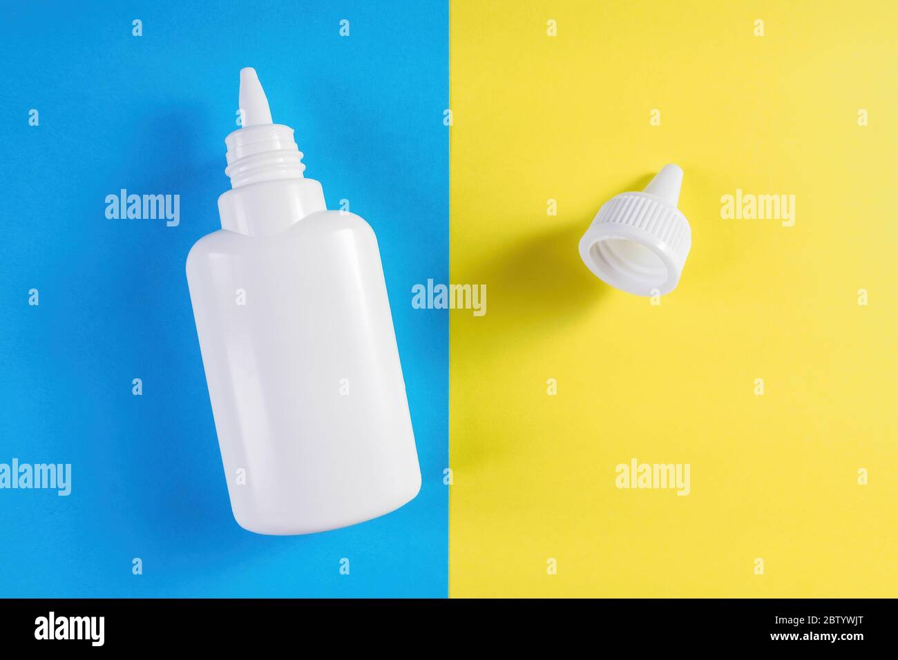 Flacon en plastique blanc et bouchon sur fond bleu et jaune. Aérosol de froid commun ou allergie, spray pour le nez, gouttes médicales. Vue de dessus Banque D'Images