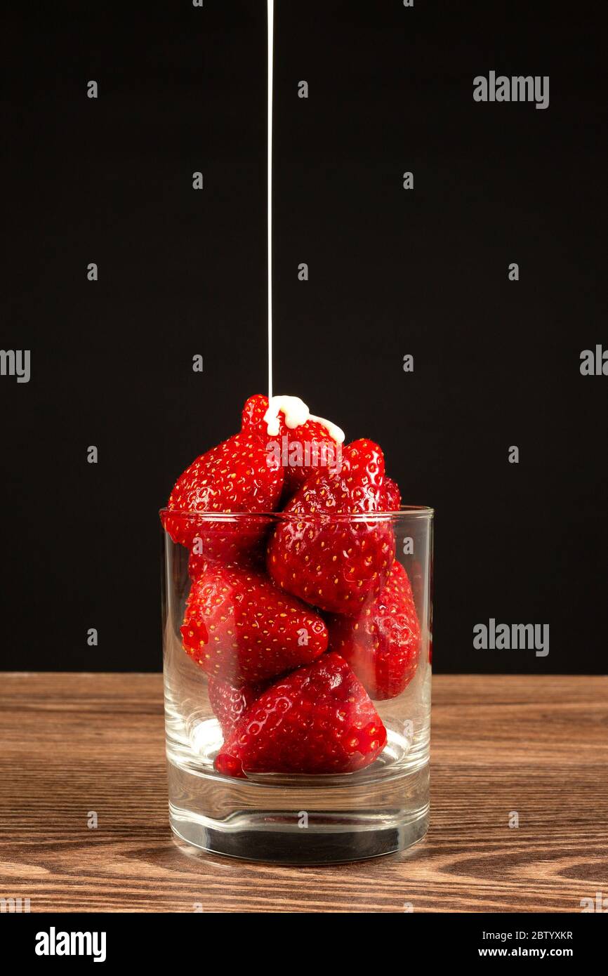 Fraises dans un verre avec une cuillère et du lait condensé sur fond sombre Banque D'Images