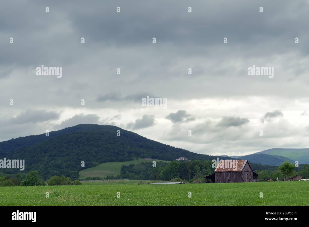 Une scène rurale représentant une ancienne grange dans un pâturage de foin avec nuages de tempête au-dessus et des montagnes en arrière-plan. Banque D'Images