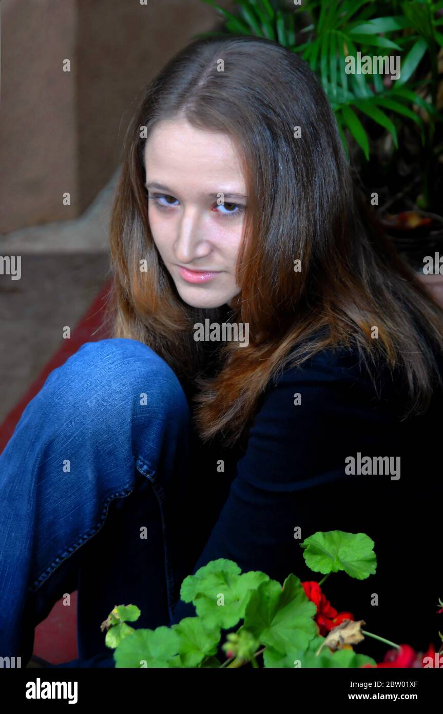 Une adolescente est assise dans son endroit isolé et privé dans le jardin. Elle est perdue dans ses pensées pensives. Elle porte un haut à imprimé vert et un Jean Banque D'Images