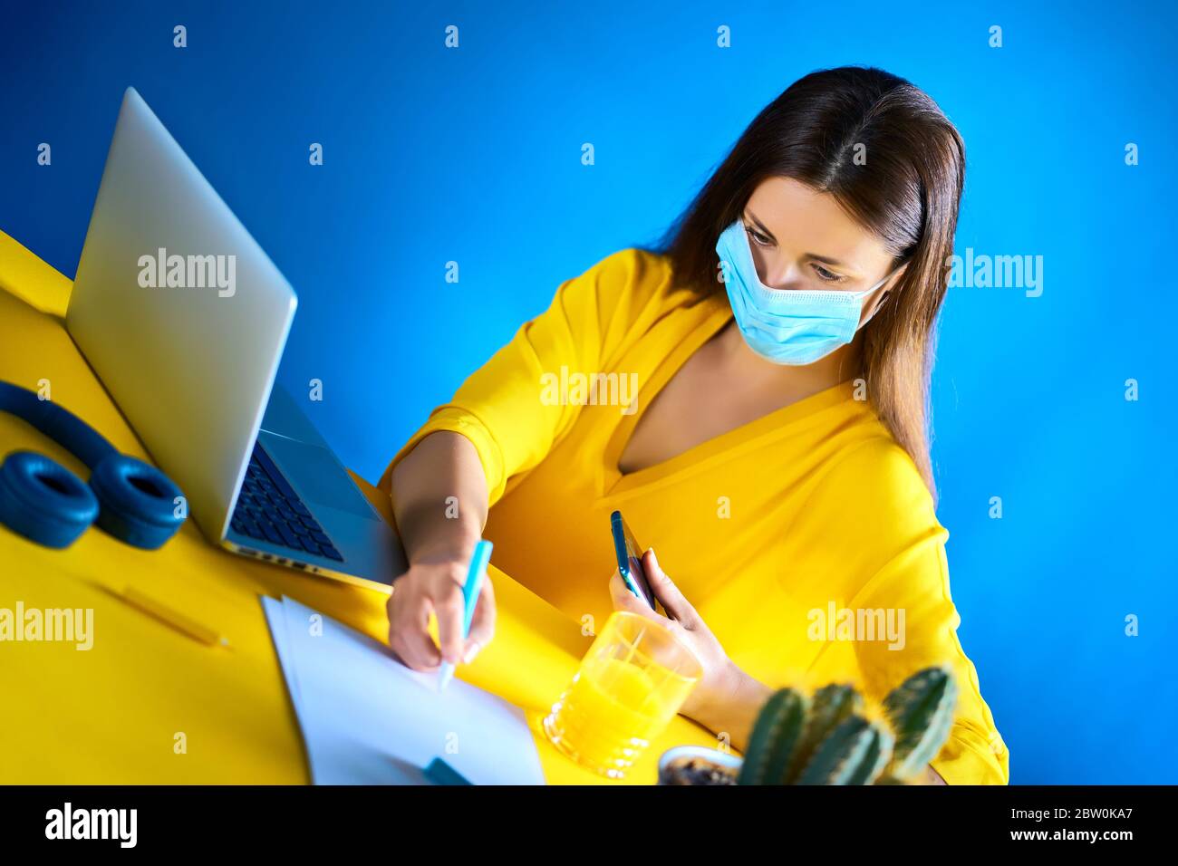 femme dans un chemisier jaune travaille à distance à la maison pendant une pandémie Banque D'Images