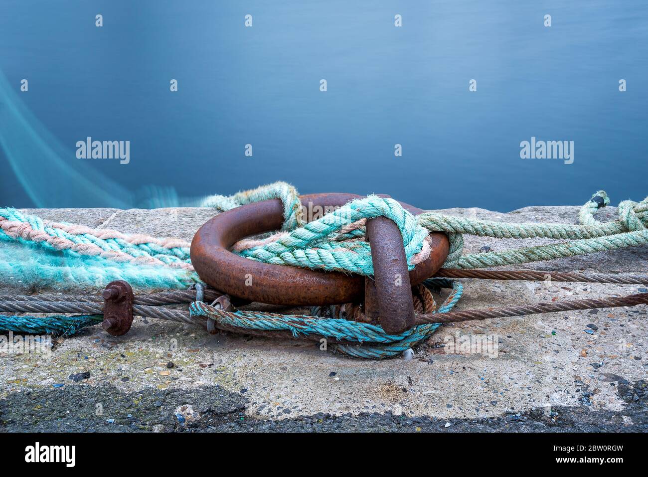 anneau d'amarrage sur le quai avec cordes et amarres serrées autour. Photo en exposition prolongée. L'eau en arrière-plan Banque D'Images