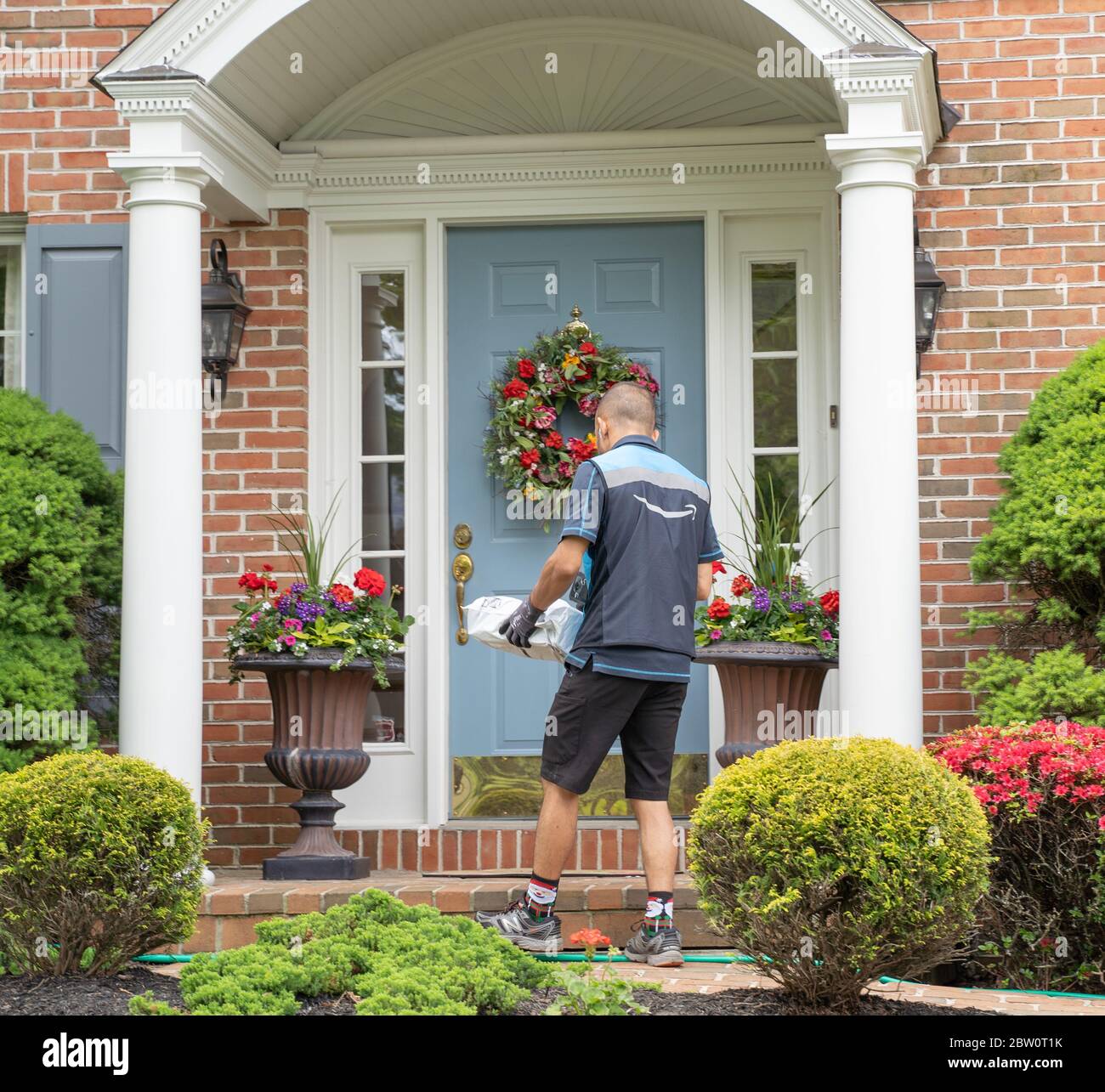 Berks County, Pennsylvanie, USA, 21 mai 2020, Amazon Delivery Person porte des gants livre le colis à la porte de la maison de banlieue. Banque D'Images