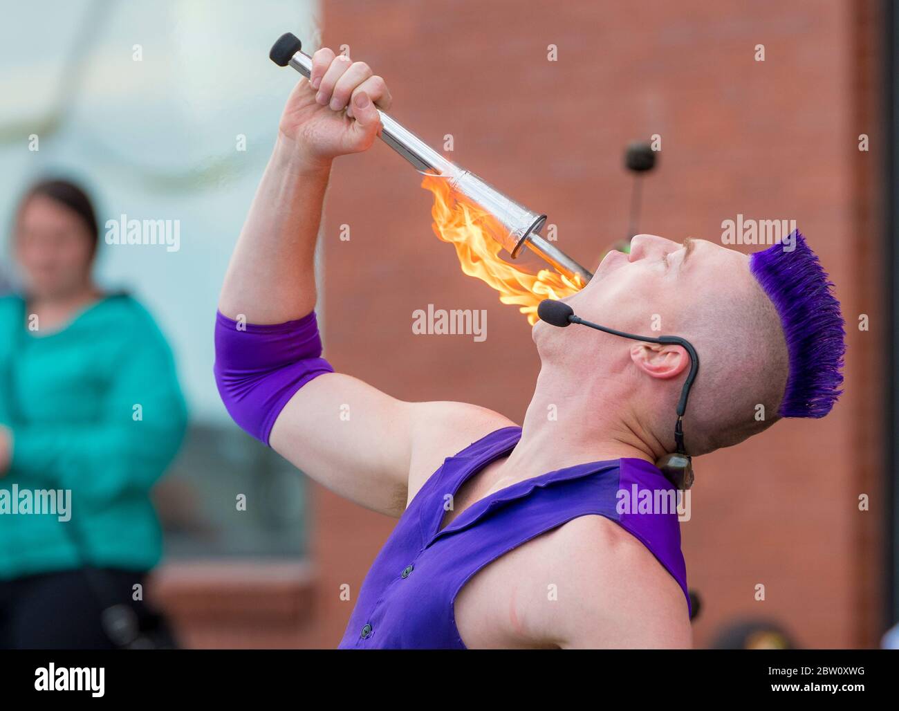 Saint John, Nouveau-Brunswick, Canada - 13 juillet 2017 : Festival annuel des Buskers. Un homme aux cheveux mohawk violets swale la fin d'un chalumeau brûlant. Banque D'Images