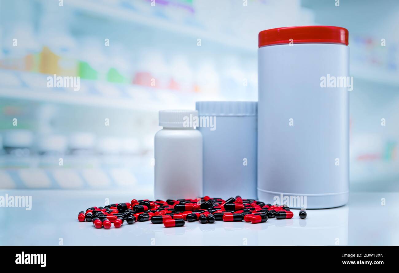 Capsules rouges-noires pilules se répandre sur le comptoir dans la pharmacie. Étiquette vierge en plastique bouteille de médicament sur fond flou de vitamines et suppléments affichage Banque D'Images