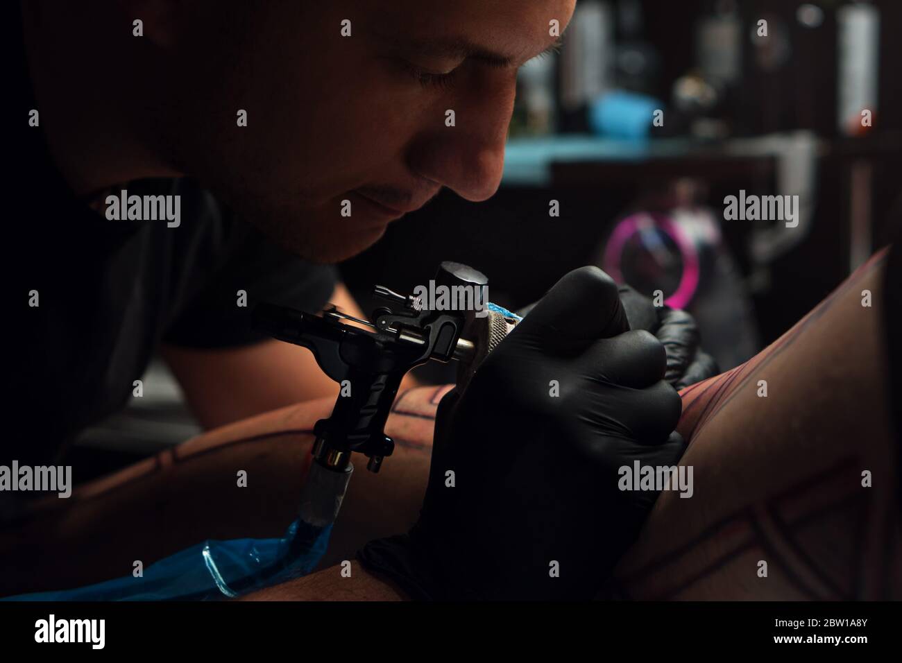 Processus de réalisation de tatouage de près. Un artiste professionnel de tatouage fait un tatouage sur la jambe jeune homme. Maître faisant tatouage dans le salon. Banque D'Images