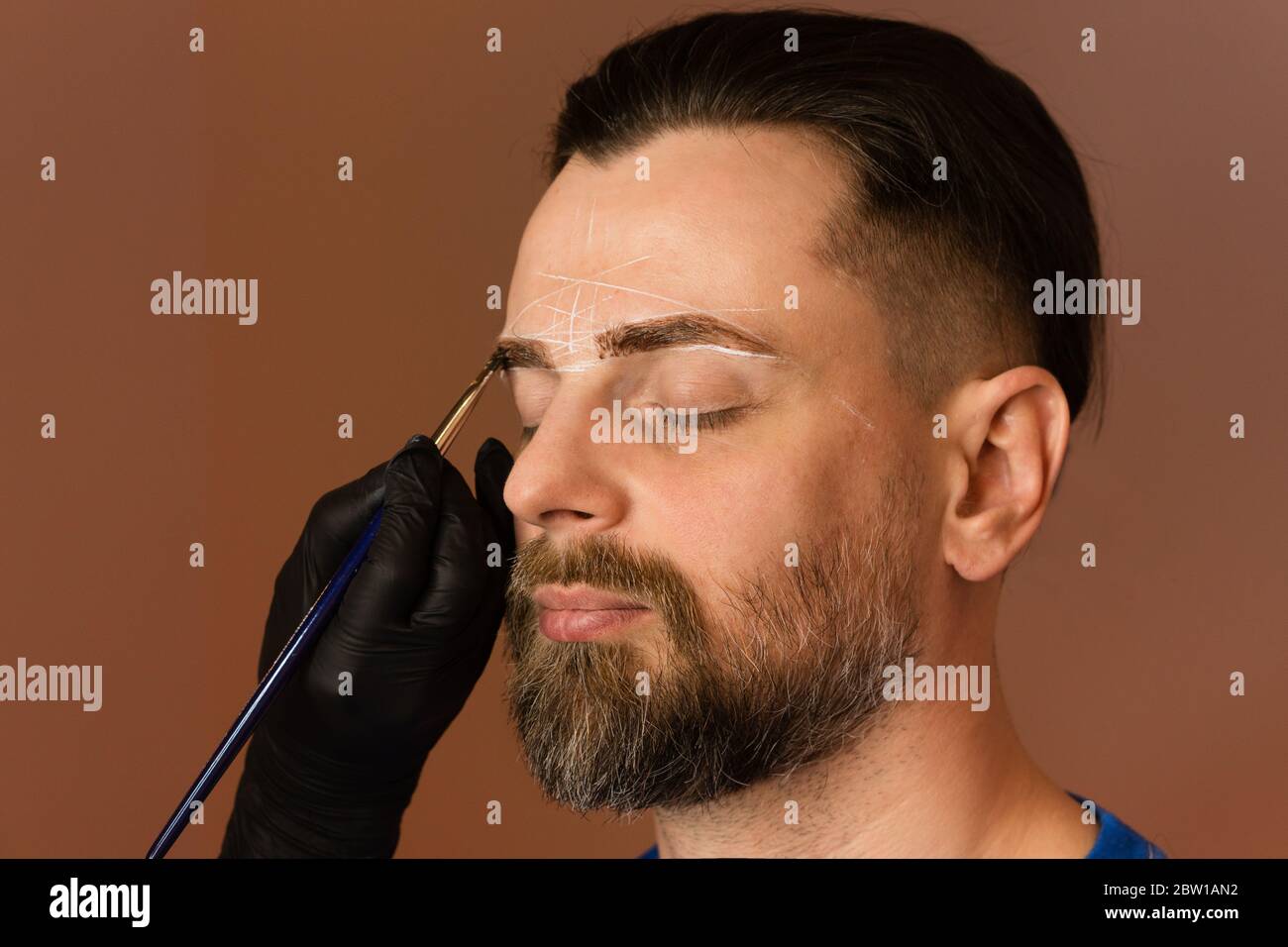 Maquillage permanent pour les sourcils. Coloration des sourcils. Beau homme  aux sourcils au salon de coiffure. Procédure beauté. Un homme brutal avec  une barbe obtient la procédure de correction du front. Coiffeur