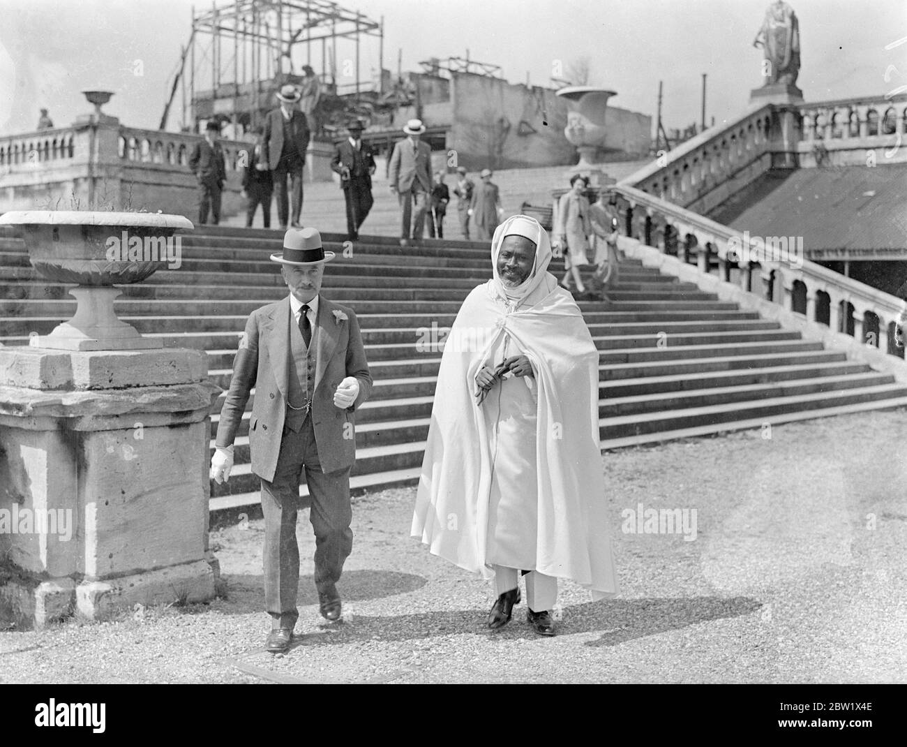 Sheikh en robes fluides au milieu des ruines du Crystal Palace. Une des ambitions de Sheikh Omar Fye, de la colonie gambienne, et de M. Arju-Adjaye, d'Ashanti, qui étaient délégués au Couronnement, a été réalisée lorsqu'ils ont effectué une visite au Palais de Cristal. Pendant de nombreuses années, ils ont voulu voir le Palais de Cristal, et ils ont décidé d'y aller bien que le palais soit maintenant en ruines après le feu désastreux. Ils ont été montrés par Sir Henry Buckland, directeur général du Palais. Spectacles photo: Sheikh Omar Fye de Gambie, en robes coulant, avec Sir Henry Buckland, directeur général, au Palais de Cristal. 4 juin 1937 Banque D'Images